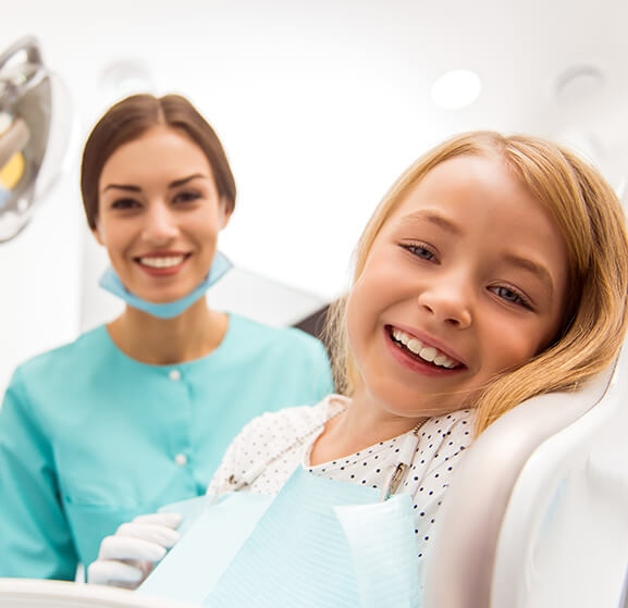 smiling girl sitting in a dental chair next to her dentist