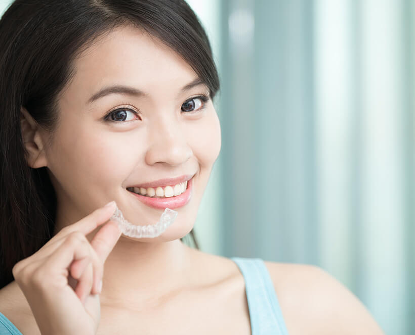 smiling woman holding up her clear aligners