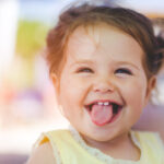 baby girl sticks out her tongue showing off two front baby teeth