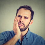 bearded man holds his jaw with a sore tooth