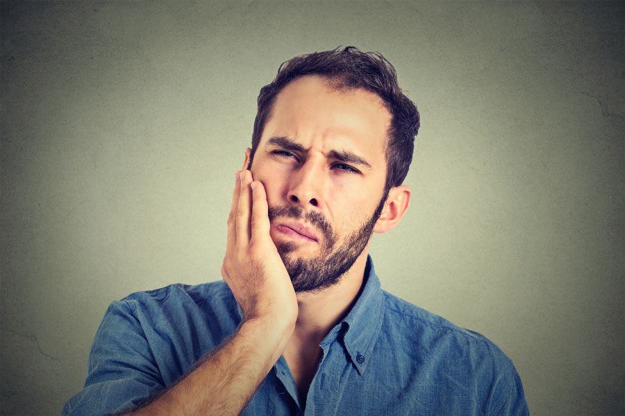 bearded man holds his jaw with a sore tooth