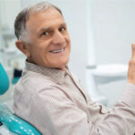 senior man gives a thumbs up sitting in the dentist chair after a successful tooth restoration