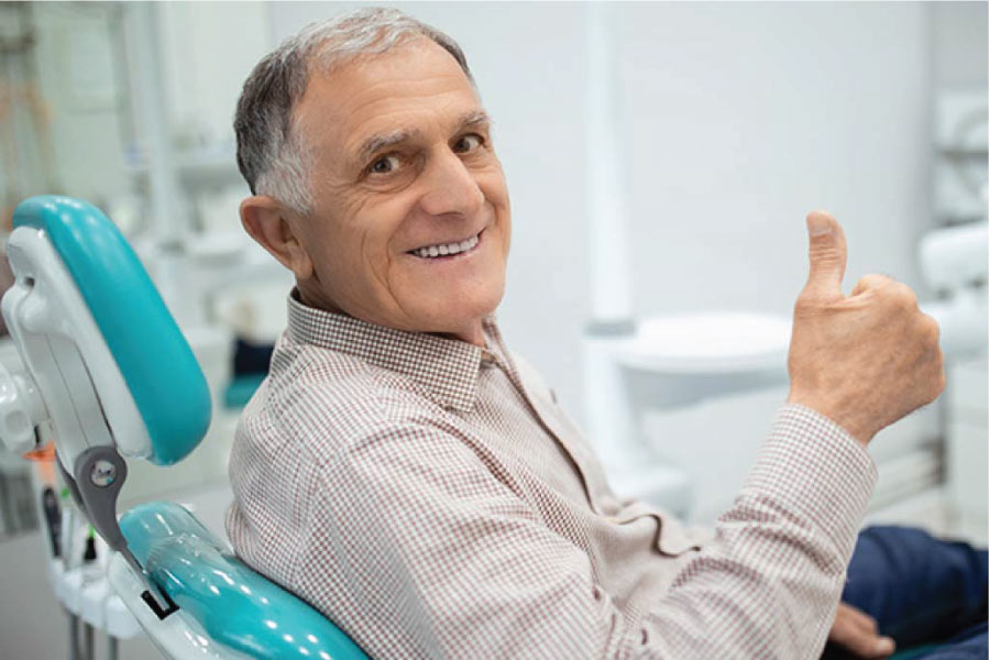 senior man gives a thumbs up sitting in the dentist chair after a successful tooth restoration