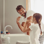 father and young daughter brush their teeth together