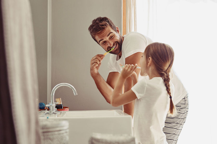father and young daughter brush their teeth together