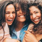 three young women hug and smile showing off their healthy teeth