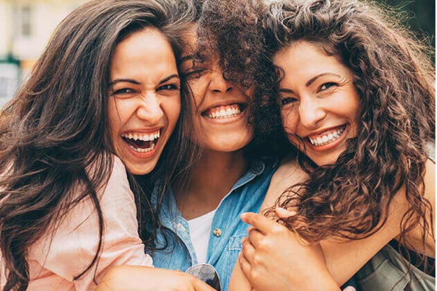 three young women hug and smile showing off their healthy teeth