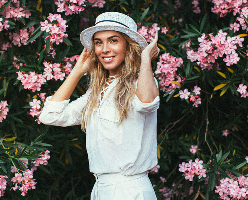 woman with hat on smiling in front of flowers