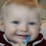 blue eyed baby boy with a toothbrush in his mouth