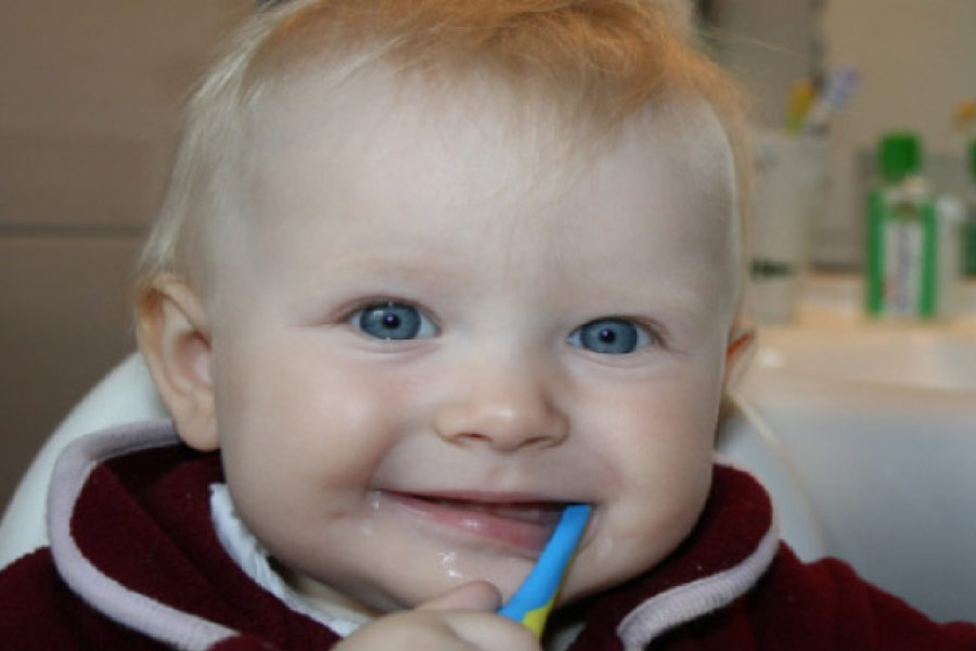 blue eyed baby boy with a toothbrush in his mouth